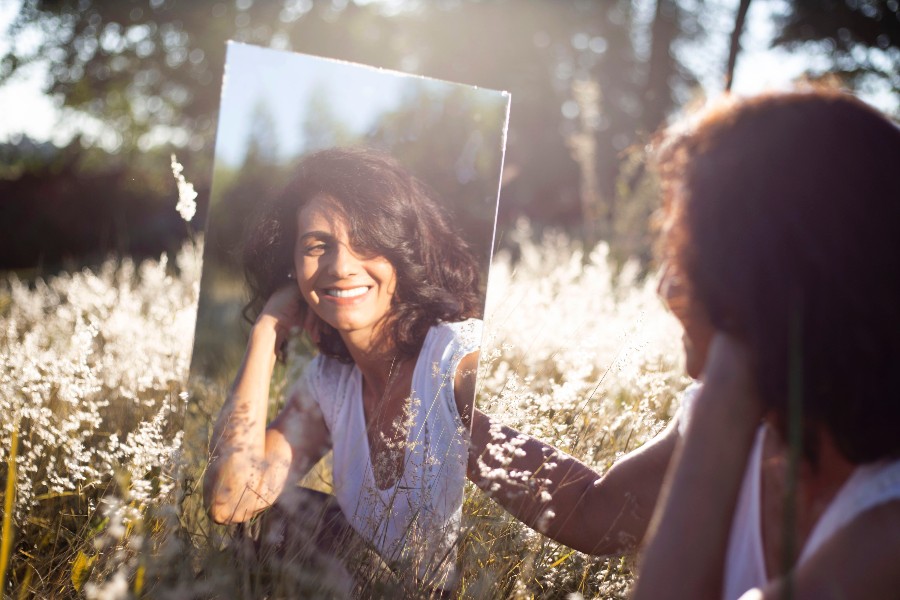 woman smiling at reflection of mirror she's holding in an open field