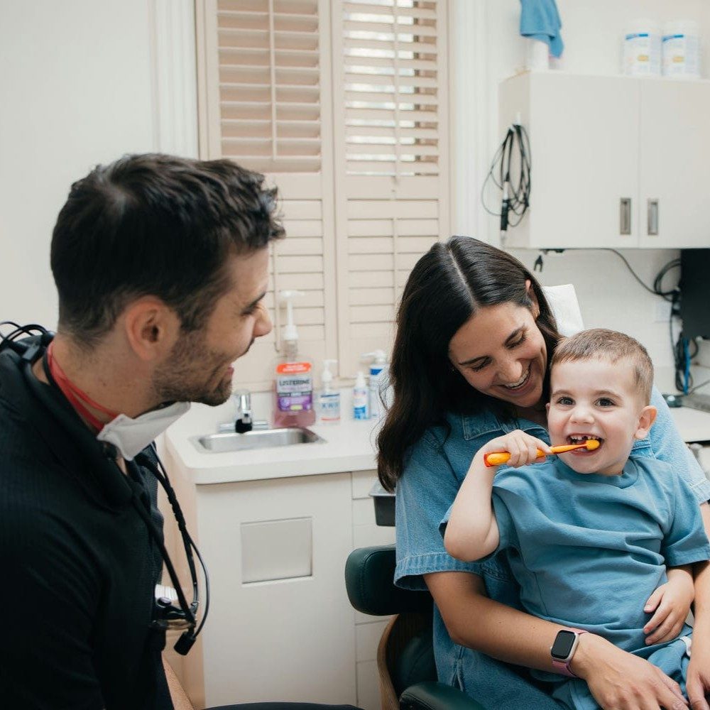 Markham family dentist with a mother and her two young sons as the toddler practises brushing