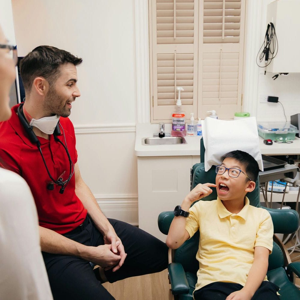 Family dentist chatting with a young boy in the treatment chair while his parent looks on