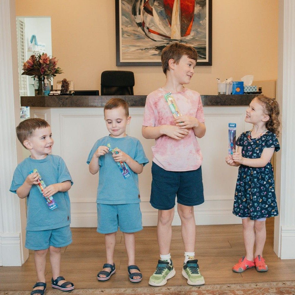 Four young patients holding new toothbrushes in the reception area after their dental visits
