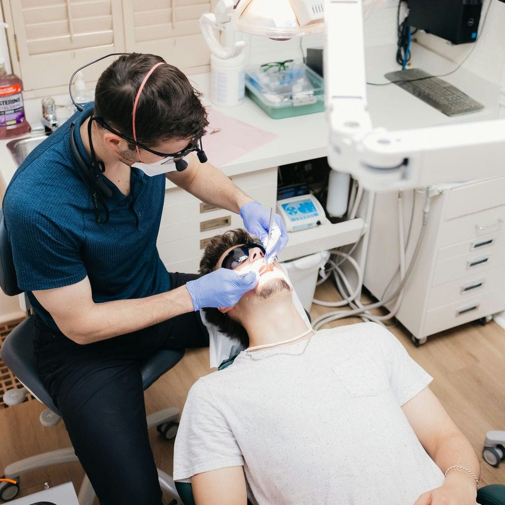 Dentist working at the back of a young adult patient's mouth during a wisdom tooth removal